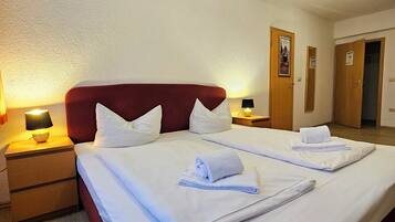 Quarto de hotel com uma cama grande, duas mesas de cabeceira com luminárias e piso de madeira.