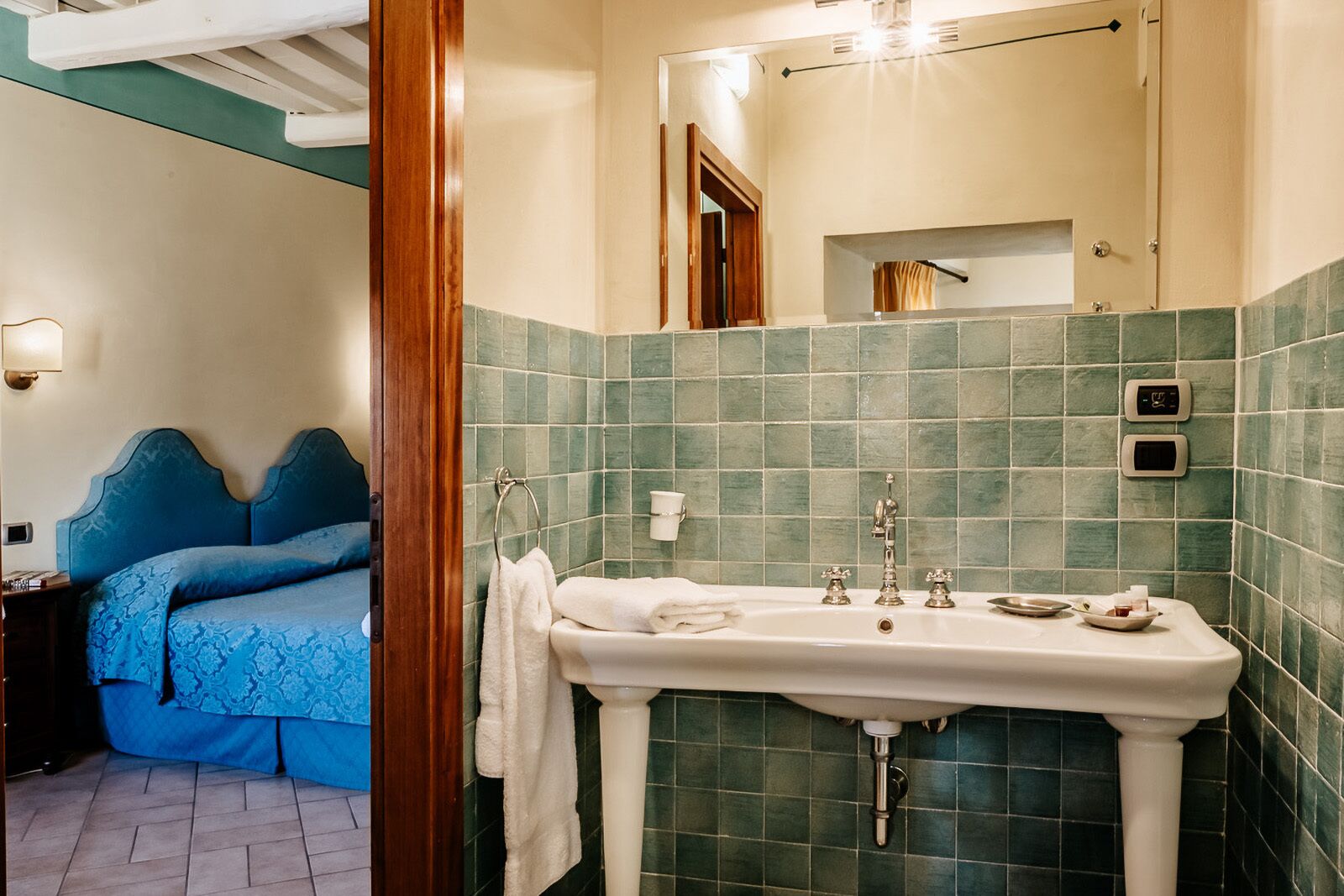 Habitación de hotel con una cama grande, baño con lavabo y espejo, y paredes de azulejos verdes.