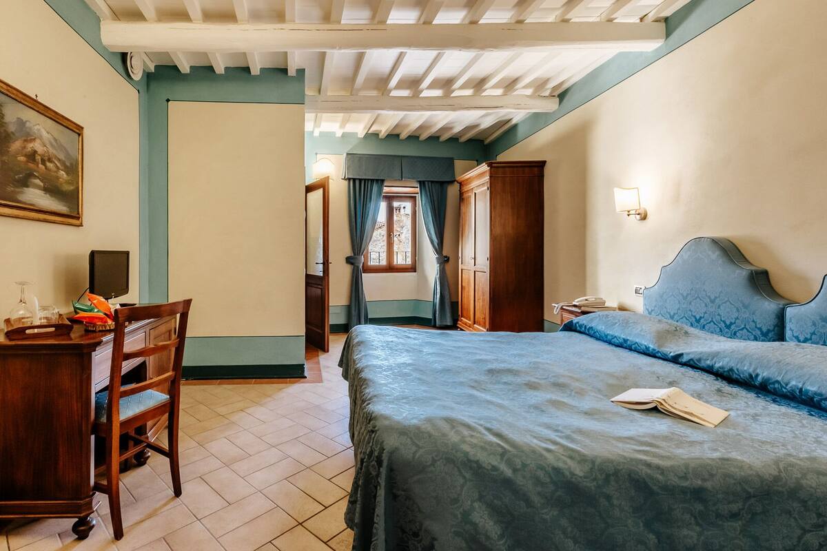 A bedroom with a bed, a desk, and a chair. There is a window with curtains and a door.