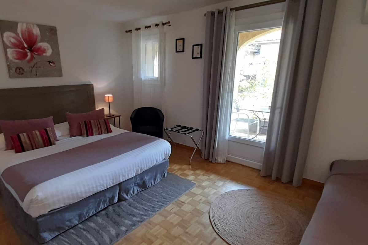 A bedroom with a large bed, bedside lamps, a chair, a window with curtains, and a painting on the wall.