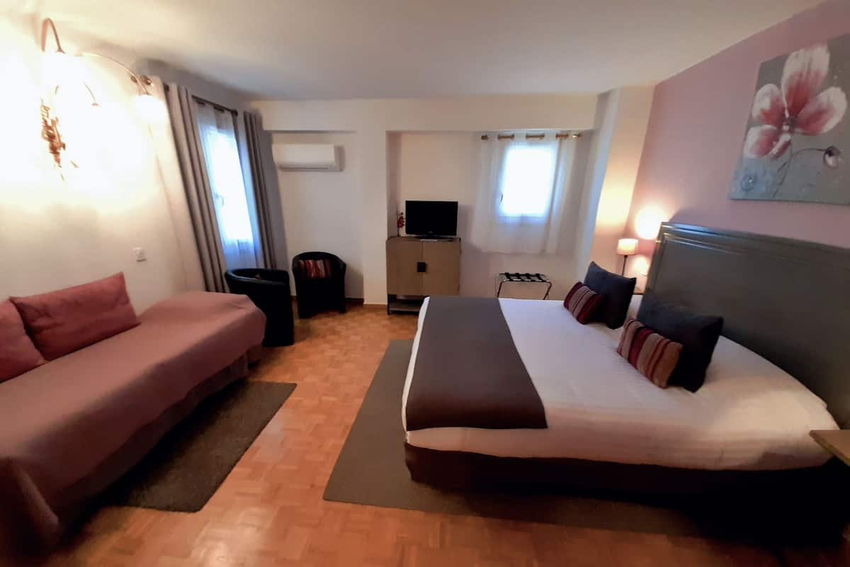 A hotel room with a bed, a sofa, a desk, a TV, and a painting on the wall.