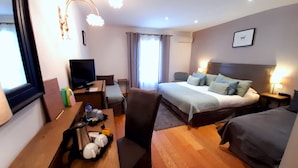A hotel room with a bed, a desk with a TV, a chair, a coffee maker, and a bedside table with a lamp. - Hôtel Le Fabian des Baux (Les Baux-de-Provence)