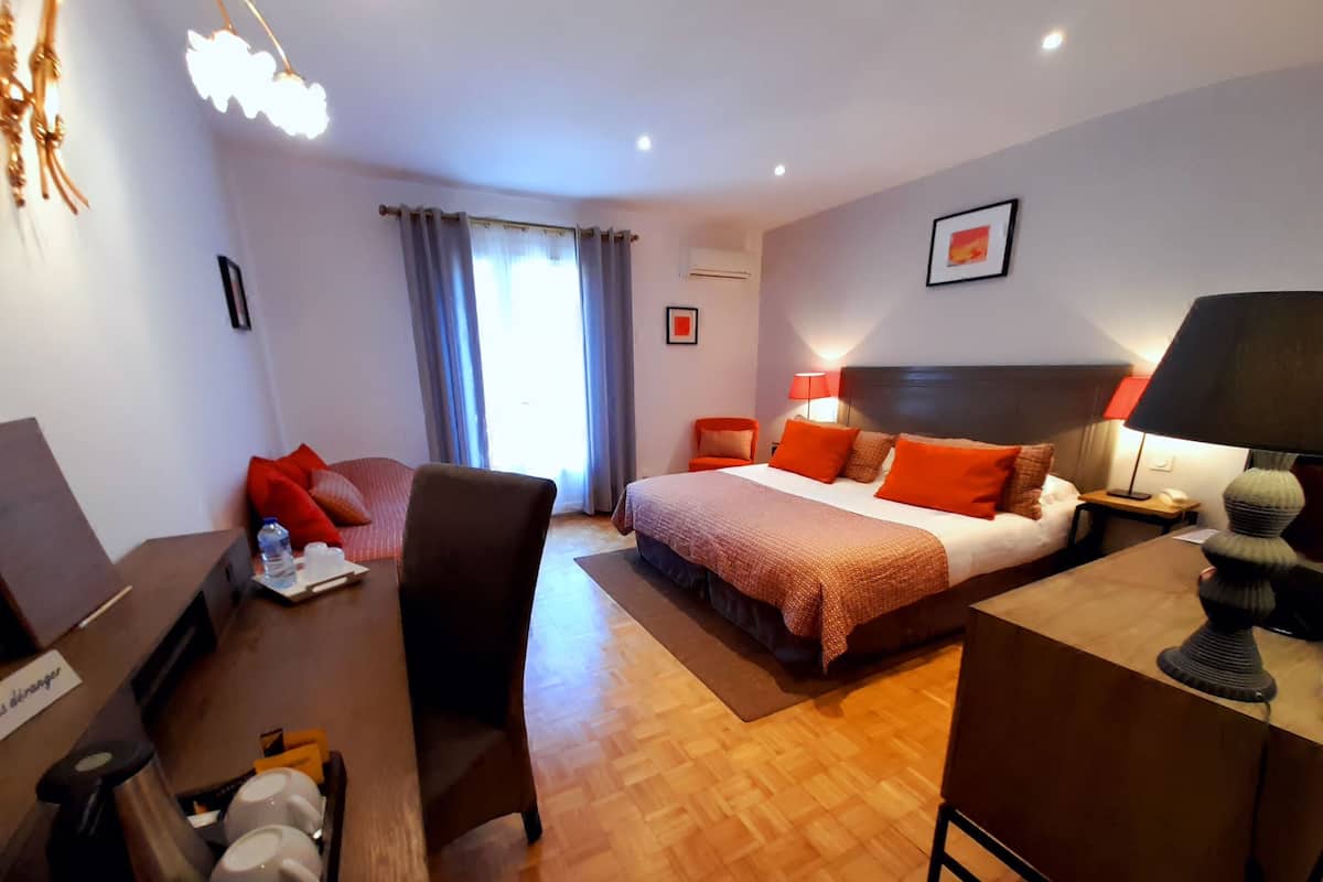 A hotel room with a bed, a desk, a chair, a coffee maker, and a lamp.