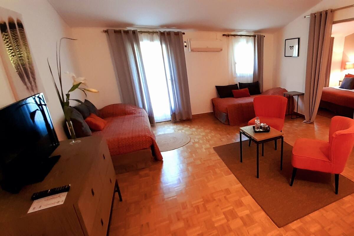A furnished living room with a sofa, armchair, and coffee table, a TV, and a desk with a chair.