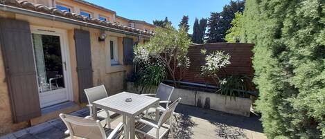 A patio with a table and chairs, a door, and a small garden area with plants and a wooden fence.