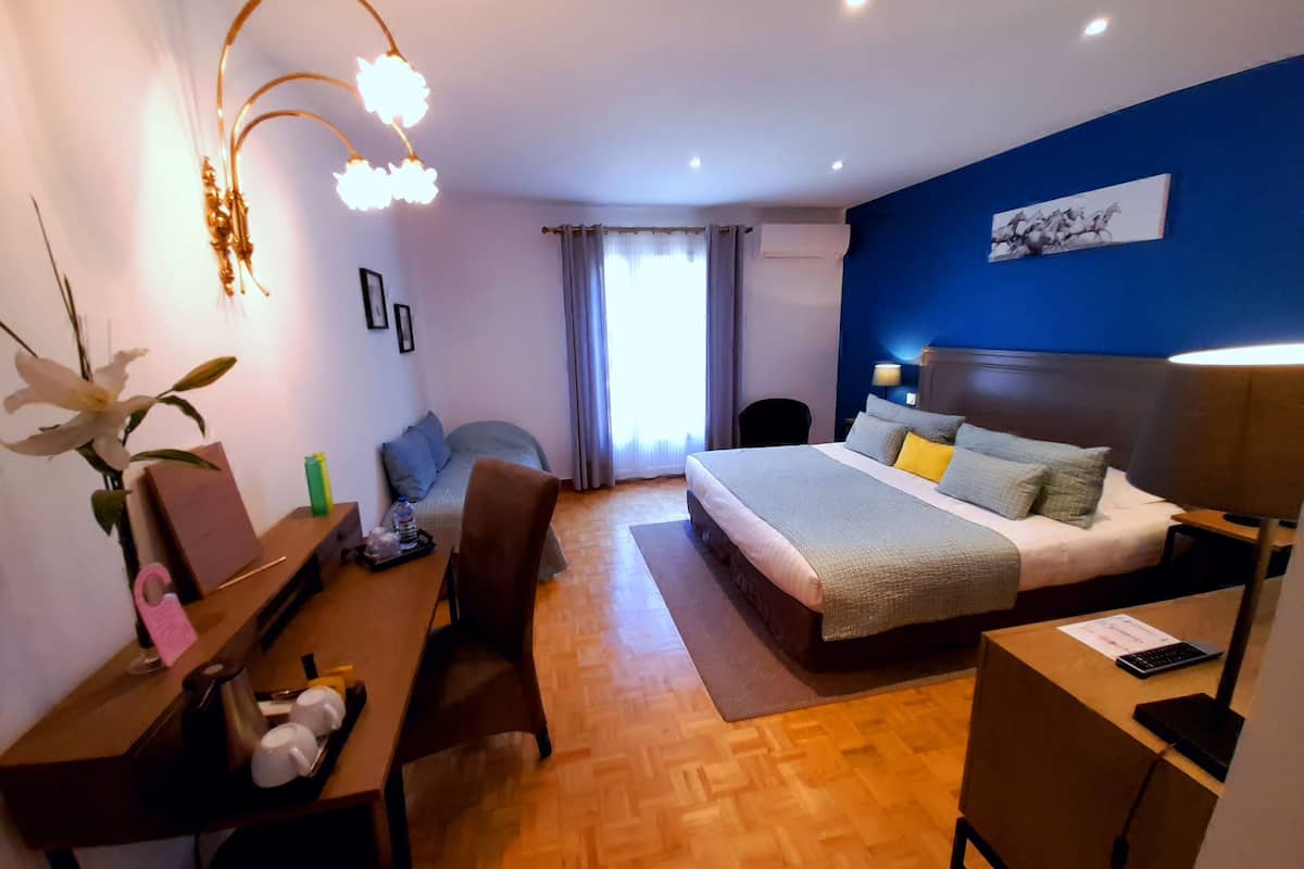 A hotel room with a bed, desk, chair, and a desk lamp.