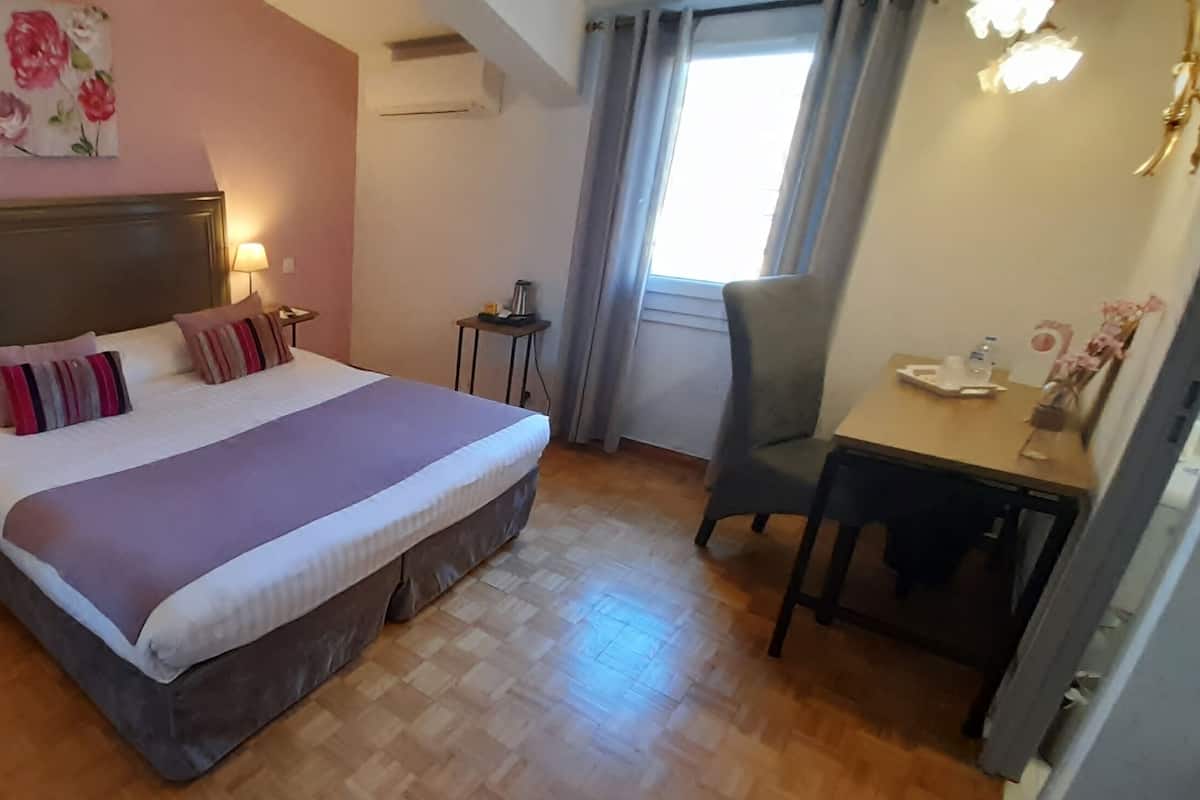 A hotel room with a bed, a desk, a chair, a lamp, and a window with curtains.
