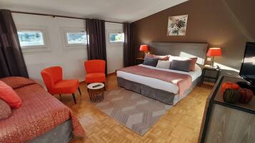 A hotel room with a bed, two orange chairs, a small round table, a TV, and a window with curtains.