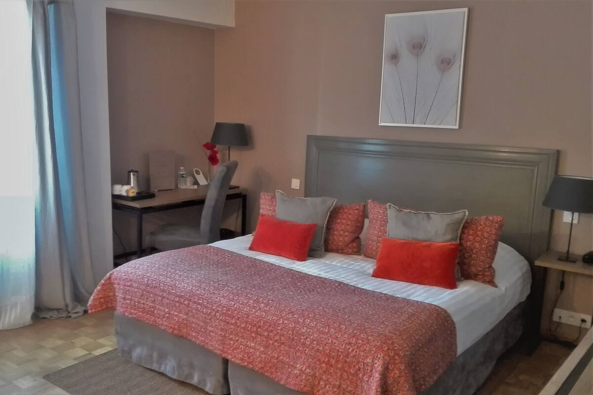 A hotel room with a bed, a desk, a chair, a lamp, and a painting on the wall.