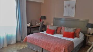 Een hotelkamer met een bed, een bureau, een stoel, een lamp en een schilderij aan de muur.