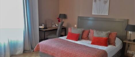 A hotel room with a bed, a desk, a chair, a lamp, and a painting on the wall.