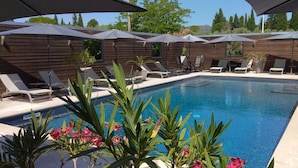 A pool area with lounge chairs and umbrellas, surrounded by wooden walls and potted plants. - Hôtel Le Fabian des Baux (Les Baux-de-Provence)