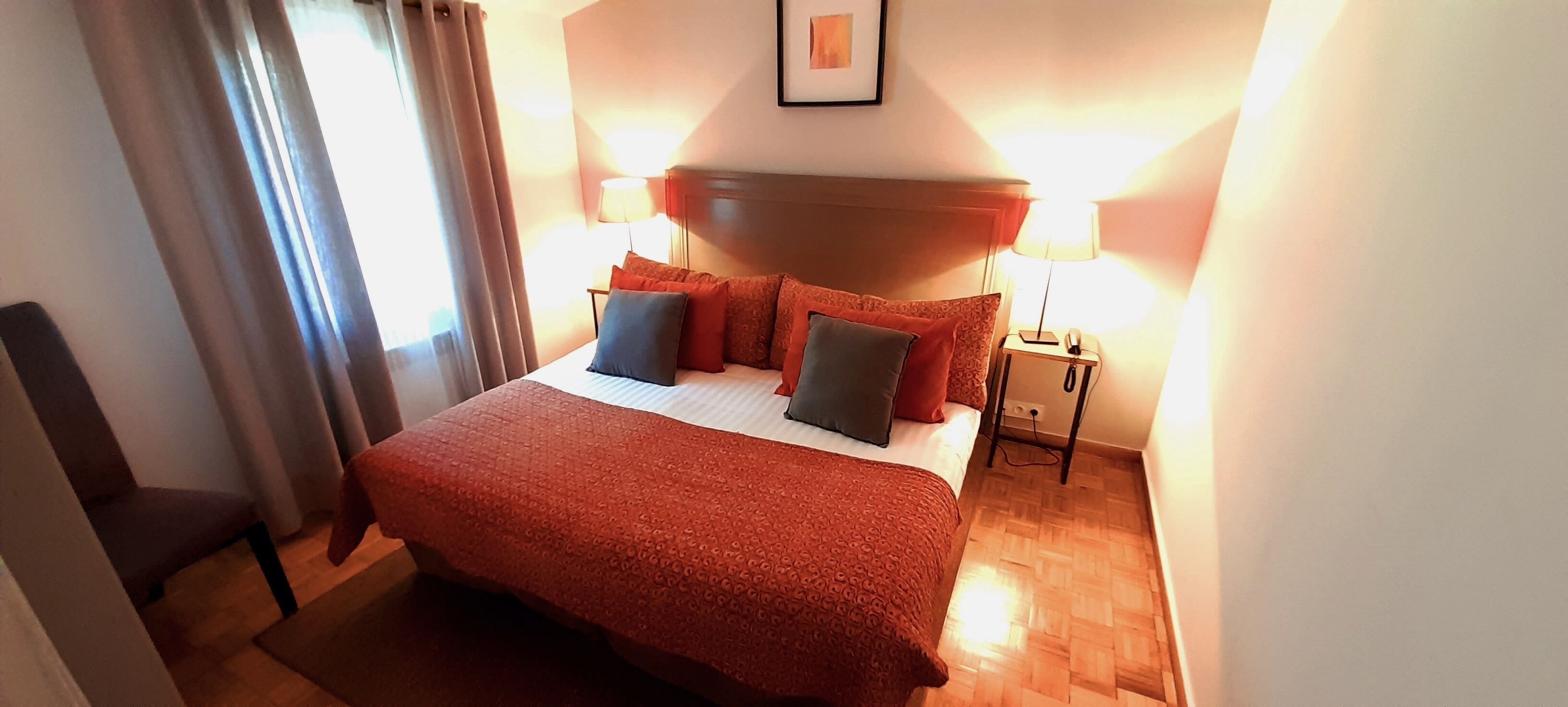 Une chambre d’hôtel avec un grand lit, deux lampes de chevet, un plancher en bois et une fenêtre avec des rideaux.
