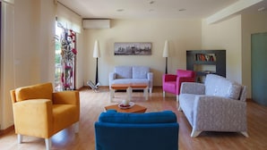 A modern living room with a sofa, armchairs, and a coffee table. There is a painting on the wall and a bookshelf with books. - Hotel Lombiña (Puebla del Caraminal)