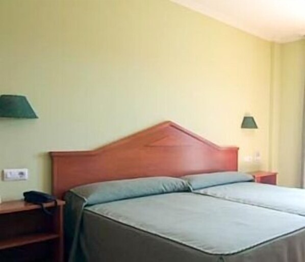 Una cama individual con cabecera de madera, dos almohadas, una mesita de noche y un pequeño mueble auxiliar.