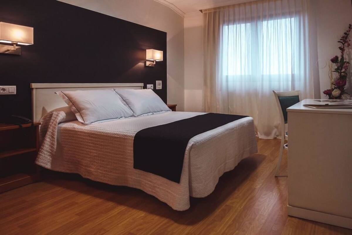 Ein Hotelzimmer mit Bett, Nachttischlampen, Schreibtisch und Kühlschrank.