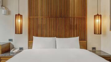 Habitación de hotel con una cama grande, dos mesitas de noche, un cabecero de madera y dos lámparas de pared.