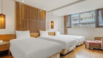 Habitación de hotel con dos camas, cabecera de madera, un escritorio, una silla y una ventana con vistas a edificios.