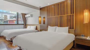 A hotel room with two beds, wooden paneling on the walls, a window with a city view, and a bedside table with a lamp.