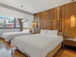 A hotel room with two beds, wooden paneling on the walls, a window with a city view, and a bedside table with a lamp. - Guide Hotel Taipei Bade (Taipei)