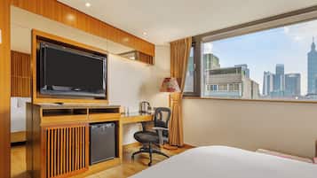 Habitación de hotel con cama, escritorio con computadora, televisor y vista a un paisaje urbano.