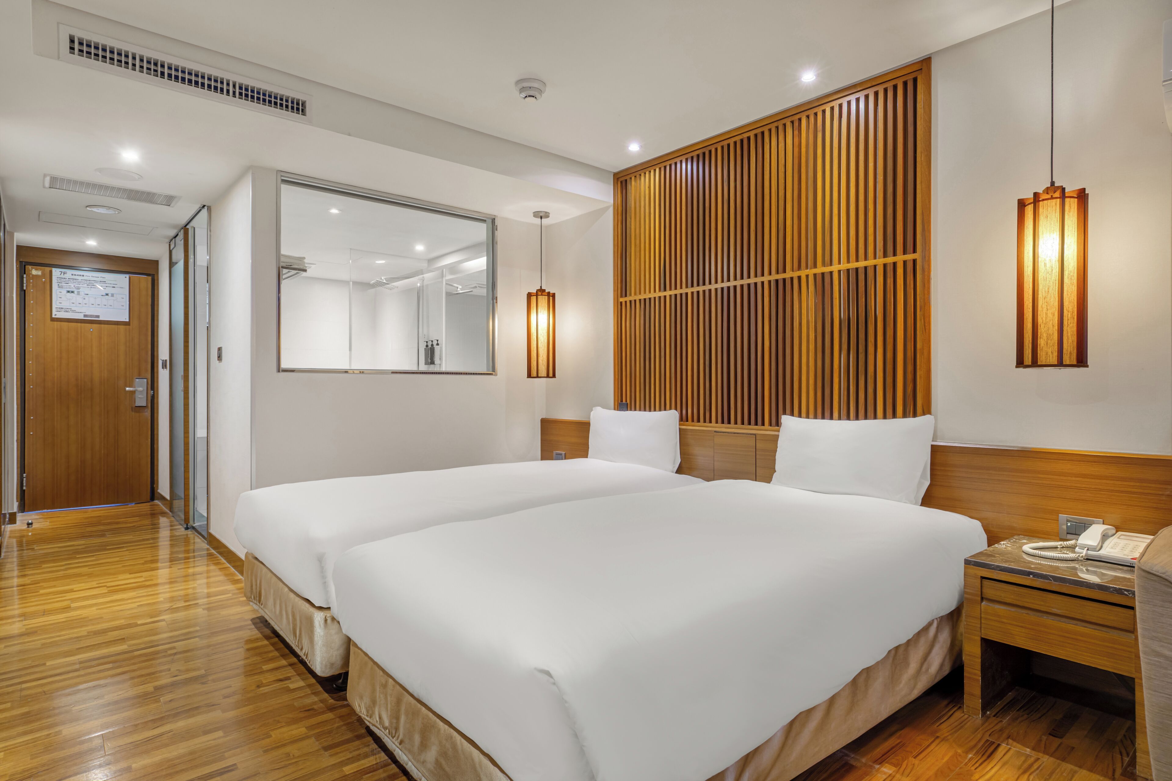 Quarto de hotel com duas camas, cabeceira de madeira, mesa de cabeceira com telefone e um espelho.