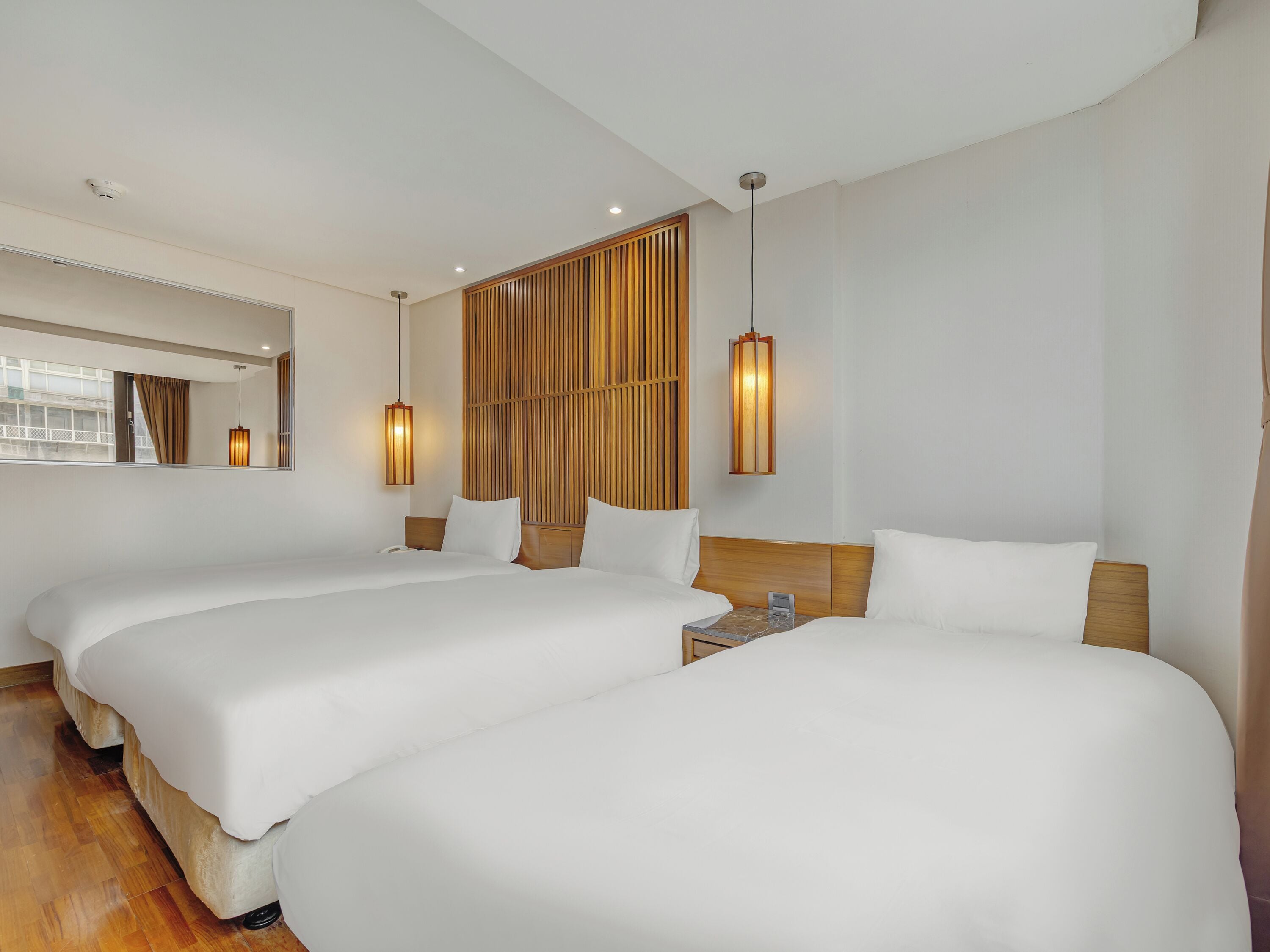 A hotel room with two beds, a wooden headboard, a nightstand, and a window with curtains.