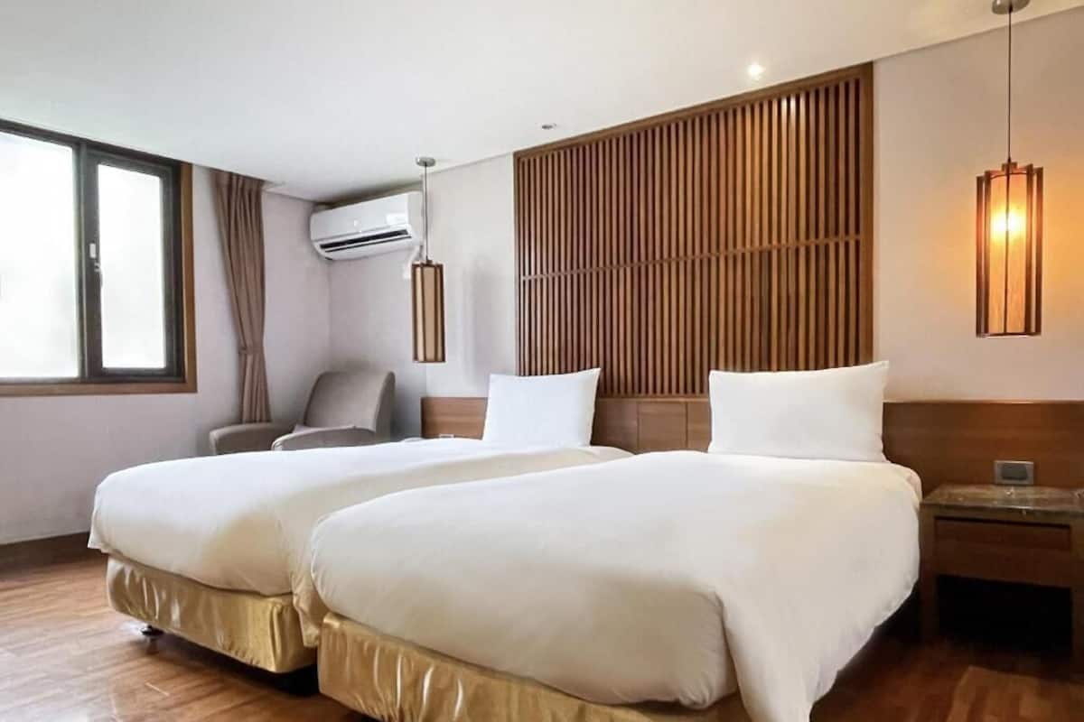A hotel room with two beds, a wooden headboard, an air conditioning unit, a chair, and a nightstand.