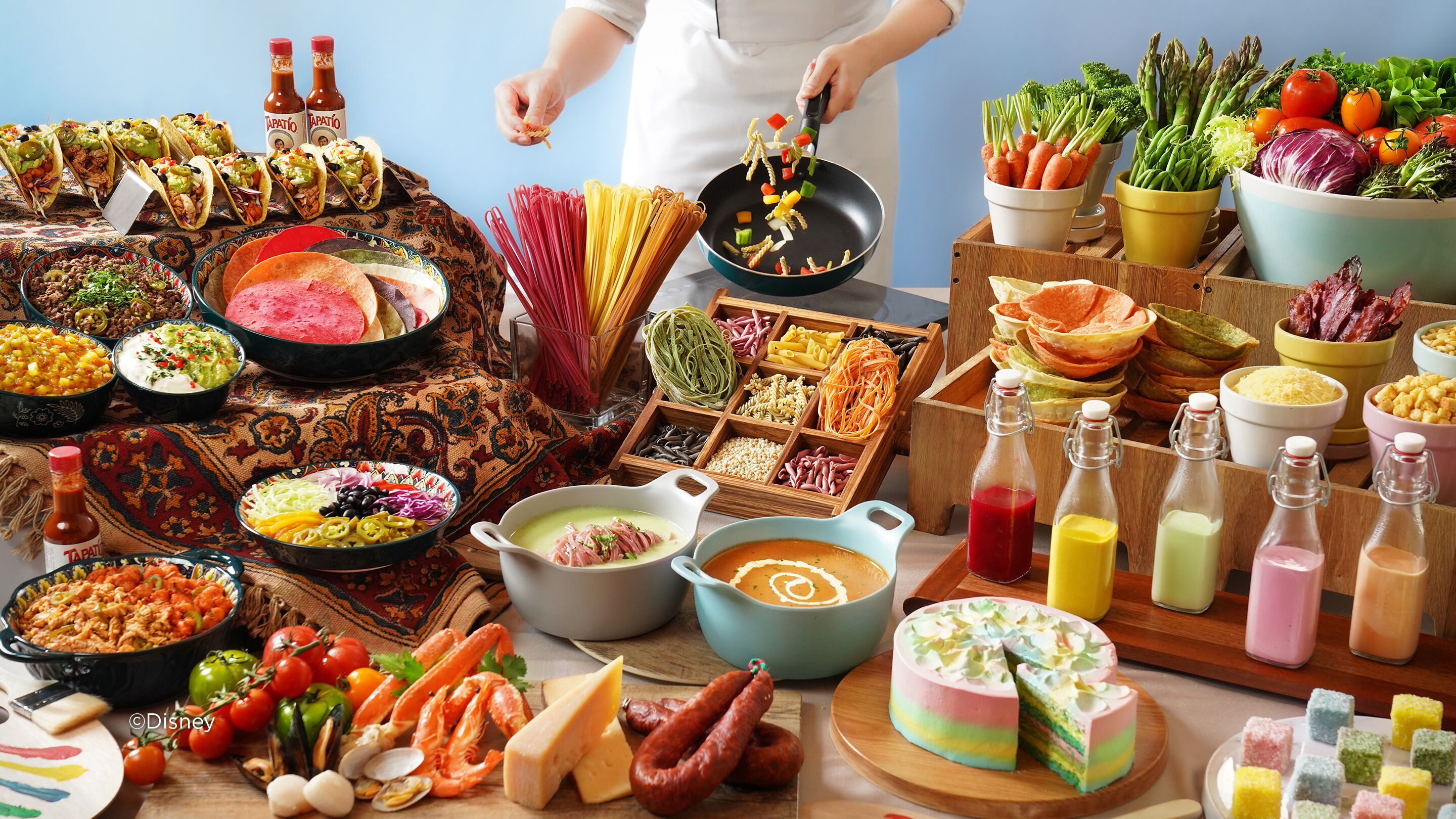 A variety of food items and condiments on a table, including tacos, pasta, and a colorful cake.