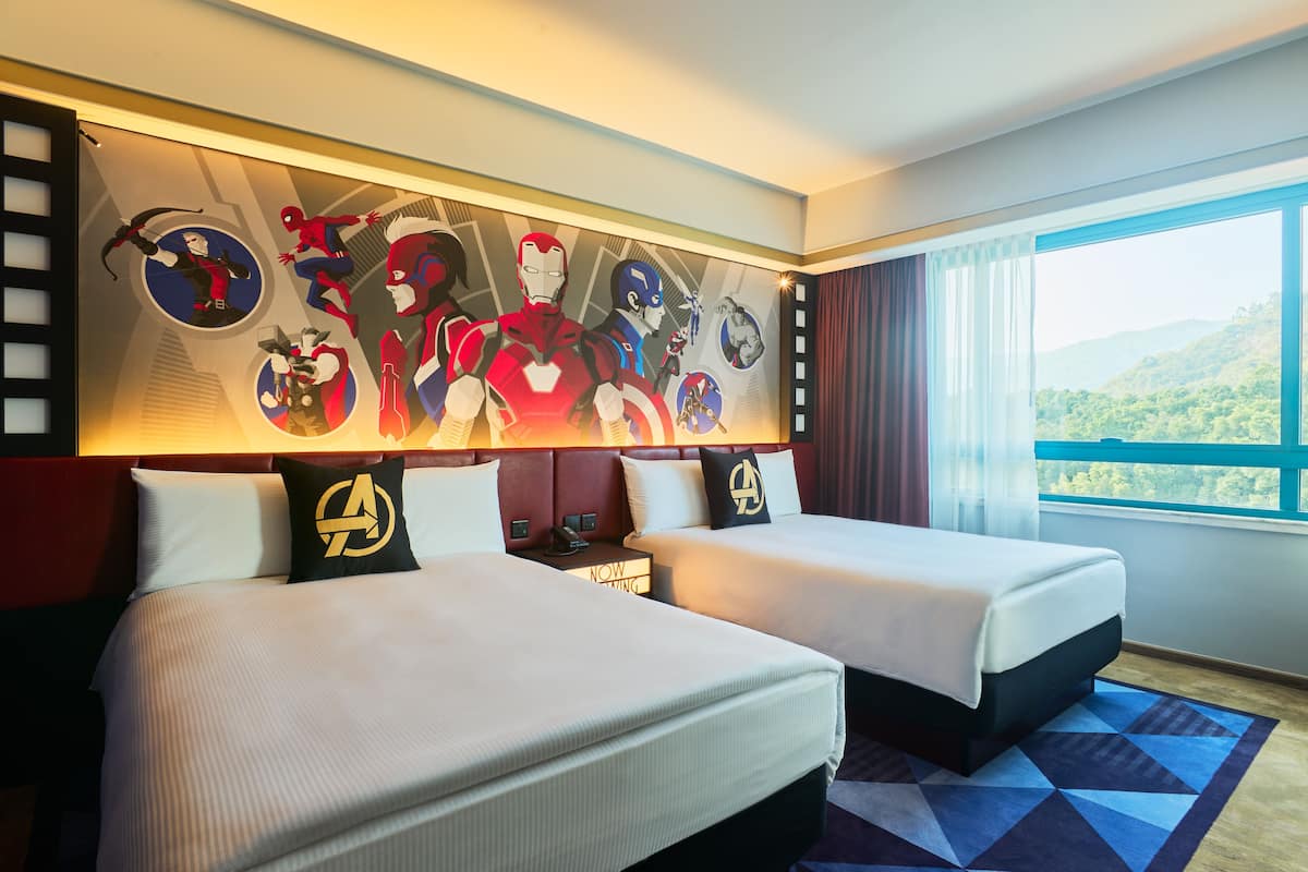 A hotel room with two beds, a large mural on the wall, and a view of the outdoors.