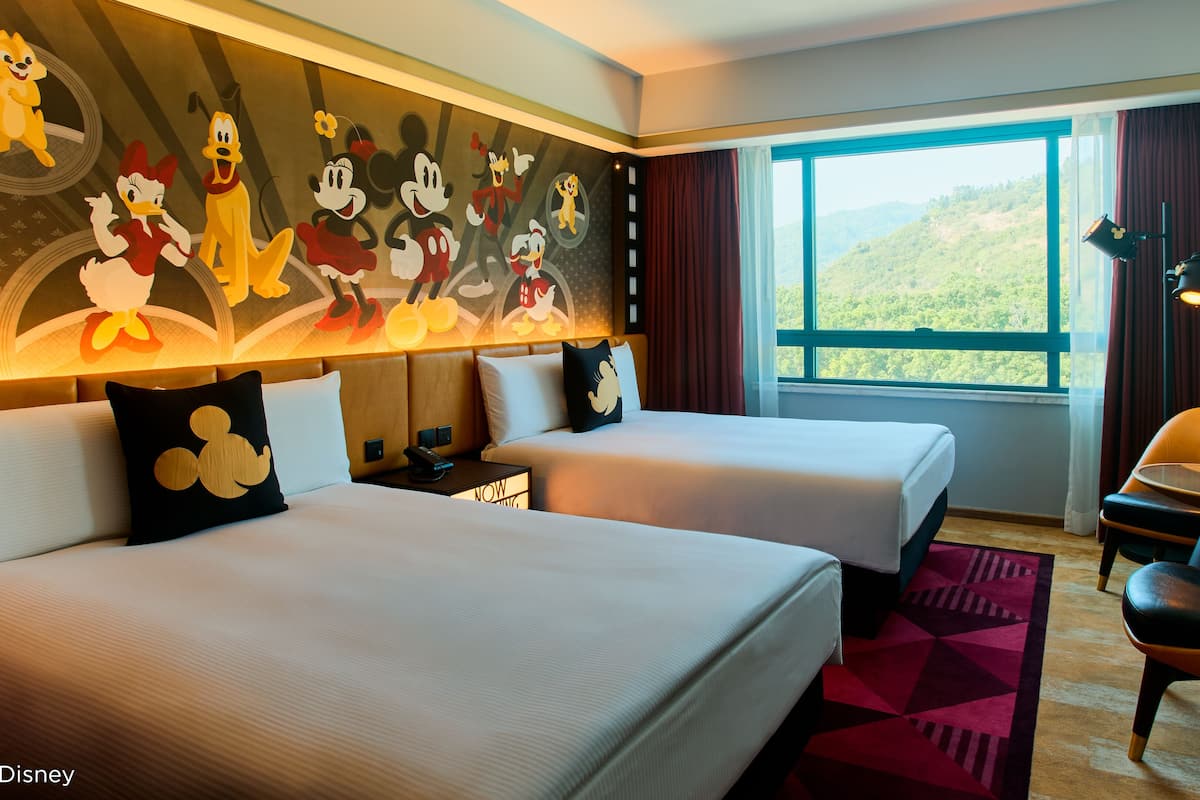 A hotel room with two beds, a desk, a chair, and a large window with a view of the outdoors.