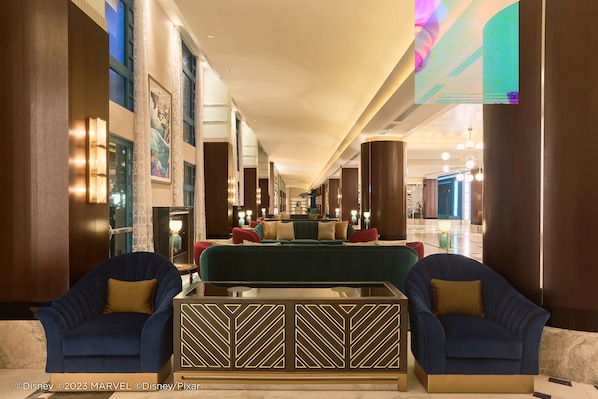 Eine großzügige Lobby mit einer zentralen Sitzecke, die ein grünes Sofa und zwei blaue Sessel, einen gemusterten Couchtisch sowie eine dekorative Wandverkleidung umfasst.