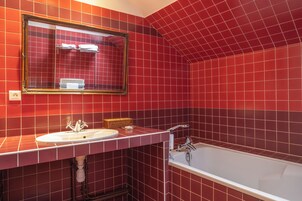 A bathroom with red tiled walls, a white sink, a mirror, and a bathtub.