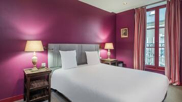 A hotel room with a large bed, two bedside tables with lamps, a window with curtains, and a view of the outside balcony.