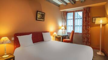 A hotel room with a large bed, two bedside lamps, a chair, a small table, and a window with curtains.