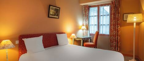 Een hotelkamer met een groot bed, twee bedlampen, een stoel, een bijzettafeltje en een raam met gordijnen.