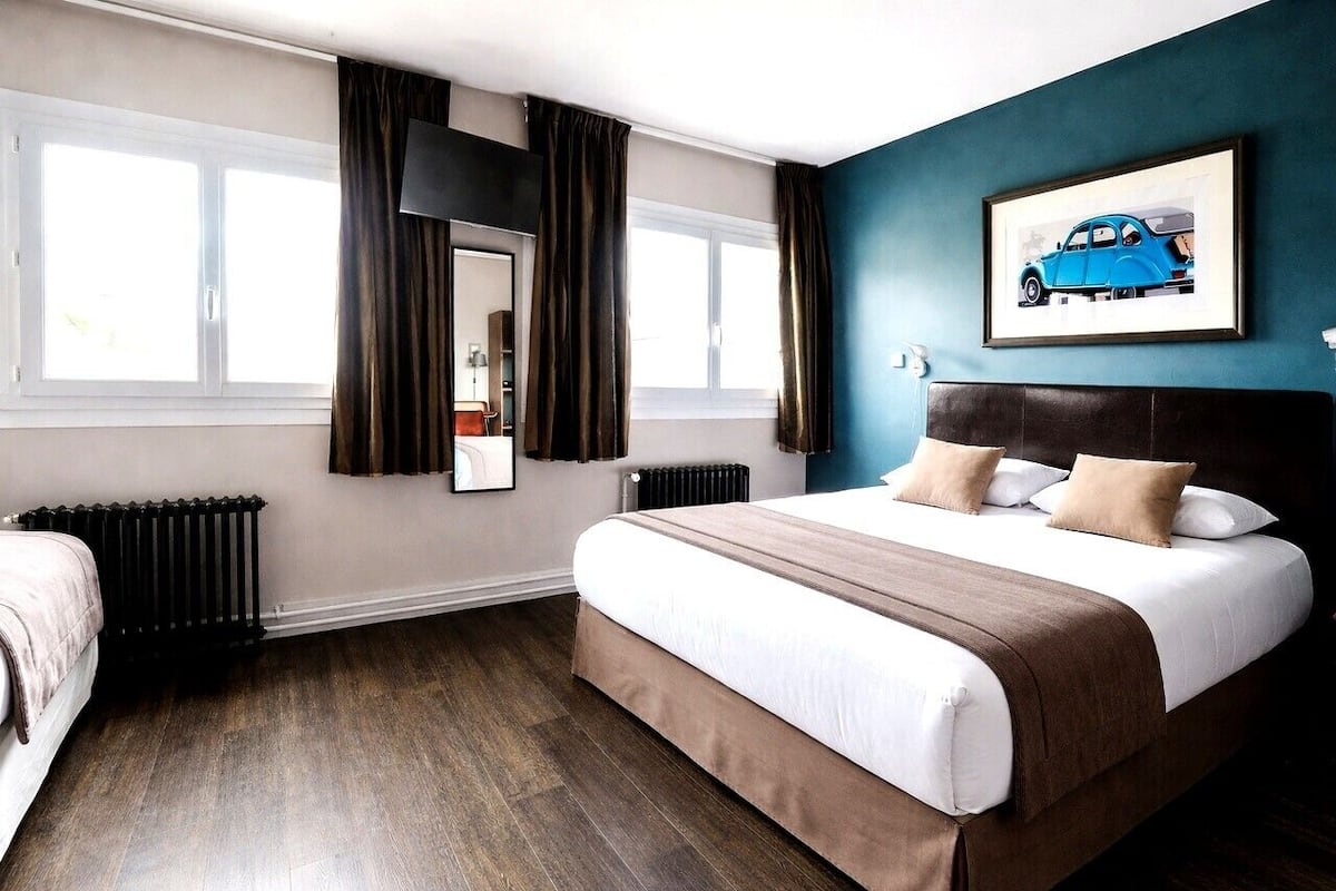 A hotel room with a large bed, a window with curtains, a radiator, and a framed picture on the wall.