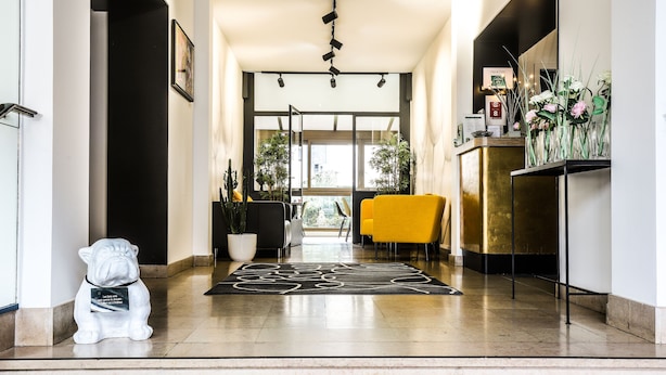A modern hotel lobby with a reception desk, a potted plant, a decorative rug, and a statue. - Hôtel Des Cèdres (Orléans)