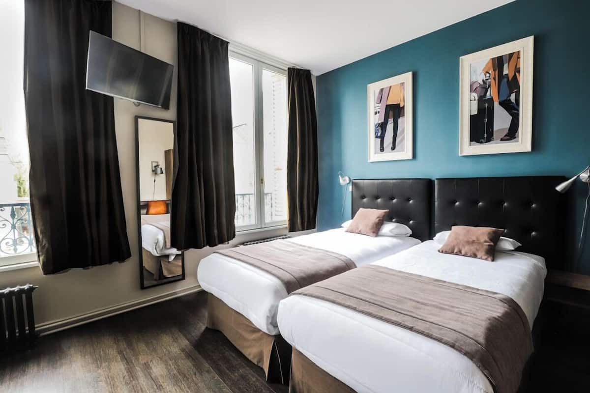 A hotel room with two beds, a TV, artwork on the wall, and a window with curtains.
