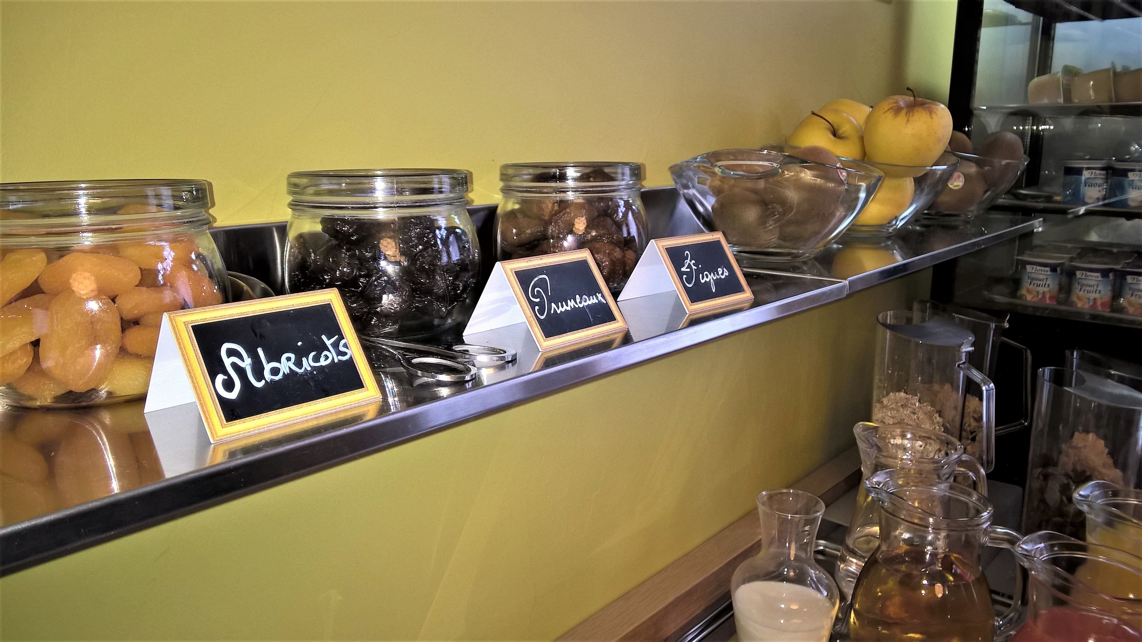 Un mostrador de buffet con frascos etiquetados de distintos alimentos y un bol de fruta.