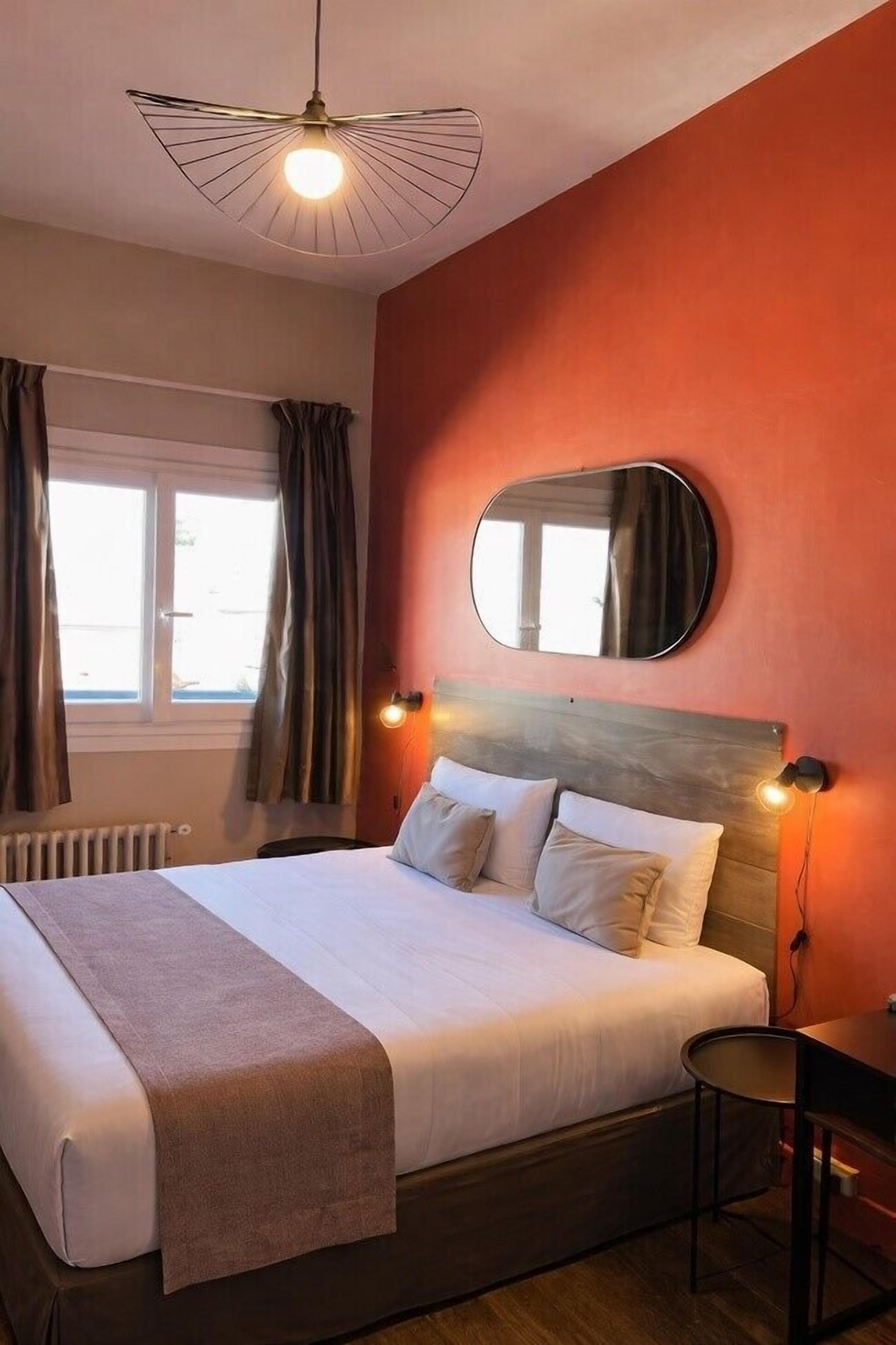 A hotel room with a bed, a round mirror, a desk, and a ceiling fan.