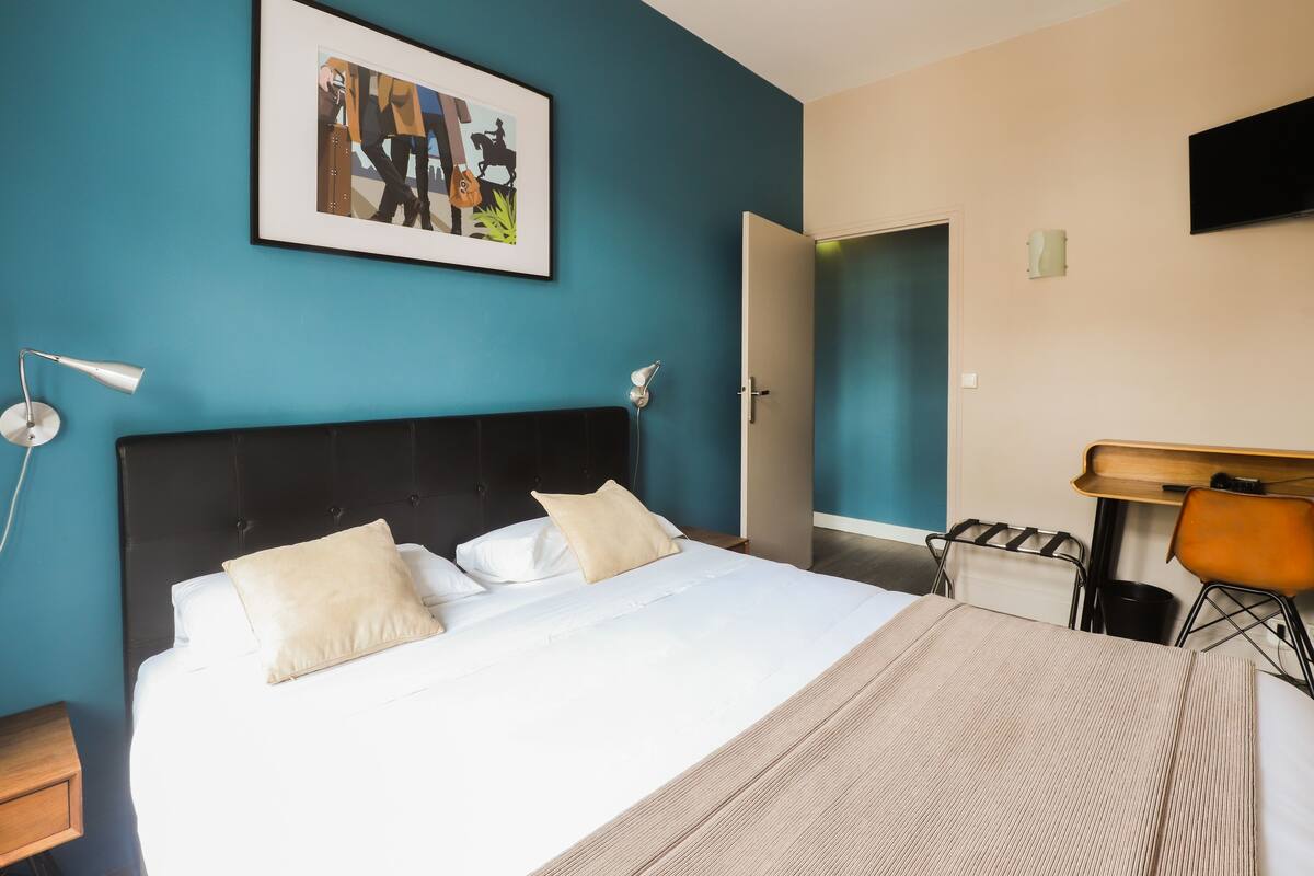 A hotel room with a large bed, a desk, a chair, and a television on the wall.
