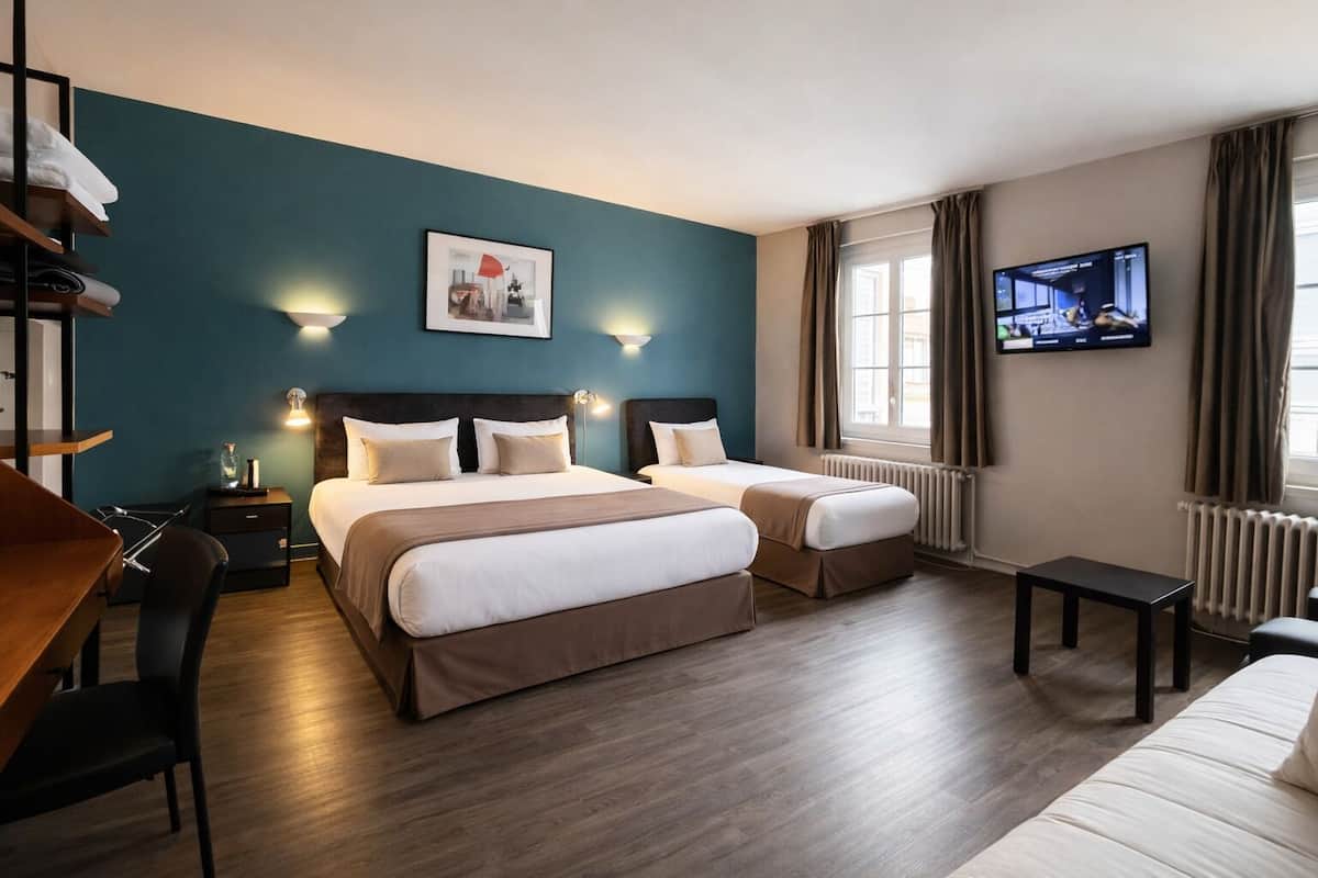 A hotel room with two beds, a desk, a chair, a TV, and a window with curtains.