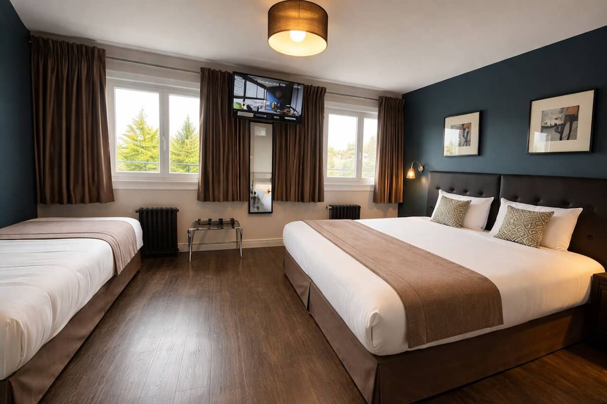 A hotel room with two beds, a TV, a window with curtains, and a radiator.