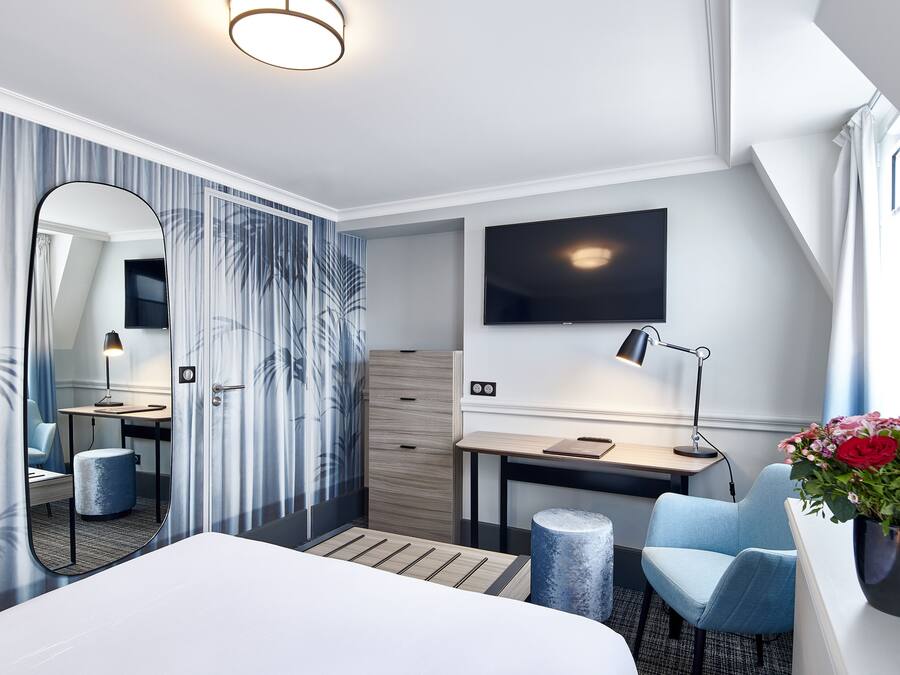 Une chambre d’hôtel moderne avec un grand lit, un bureau, une chaise, un miroir, une télévision et une plante en pot.