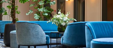 A seating area with blue upholstered chairs and ottomans, a potted plant, and a vase with white flowers.