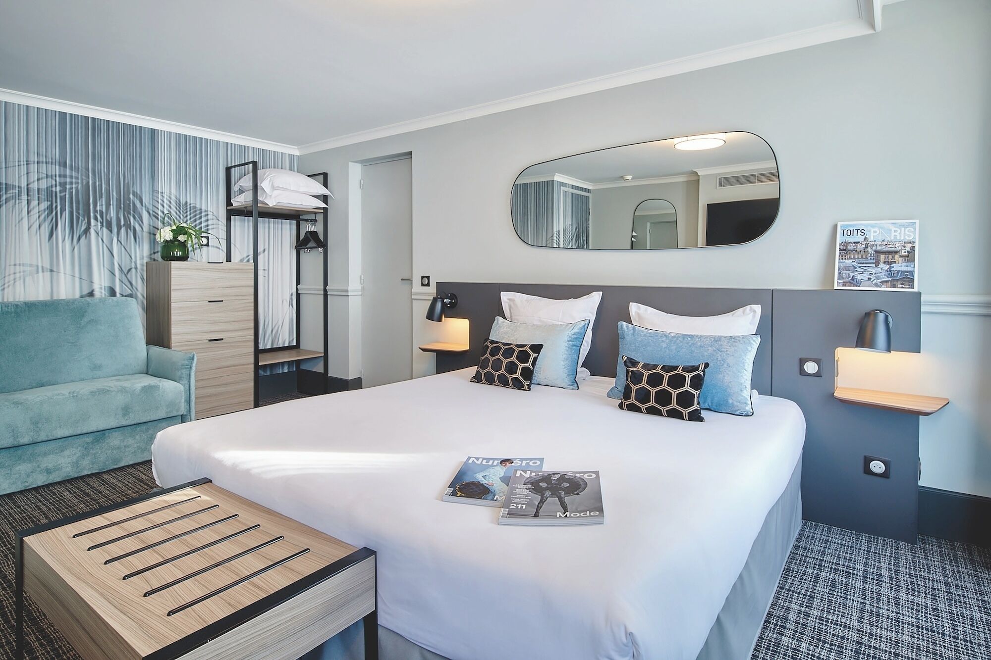 A hotel room with a bed, bedside tables, a nightstand, a mirror, a wall-mounted TV, and a window.