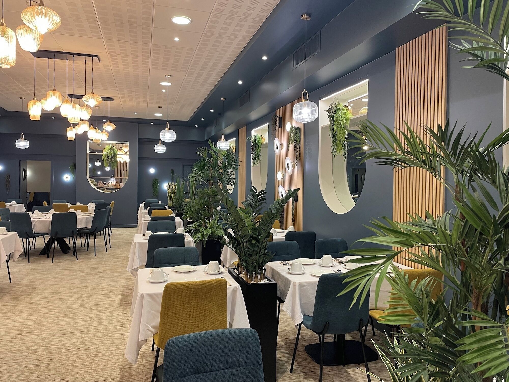 Un restaurante con mesas redondas, sillas, luces colgantes y plantas en macetas.