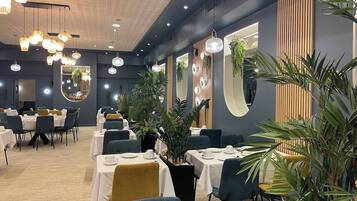 Un restaurante con mesas redondas, sillas, luces colgantes y plantas en macetas.