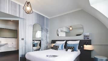 Una habitación de hotel moderna con una cama grande, un baño con lavabo y un espejo.